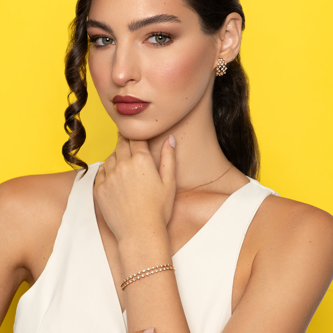 Woman wearing earrings and liali's Amara 2 Line Bangle in Rose Gold against a yellow background